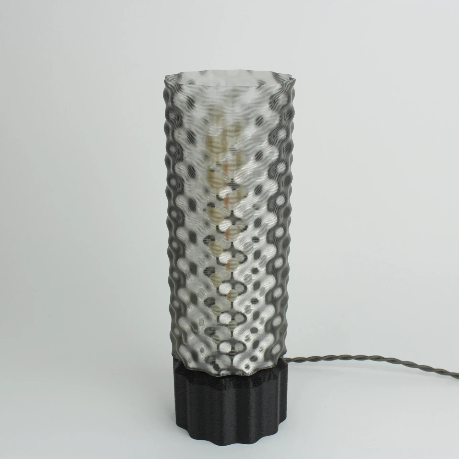 Monoprisma Fluxia Smokey Grey table lamp unlit with a translucent grey shade, black faceted base, and visible cord on a light grey background